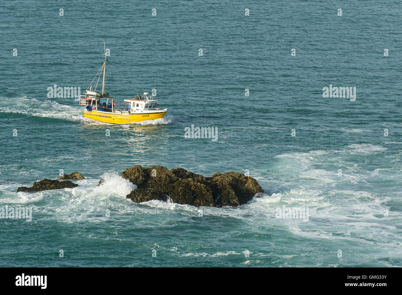 The fishing boat SS84 Three Jays steams past exposed rocks on its way back to harbour. Stock Photo