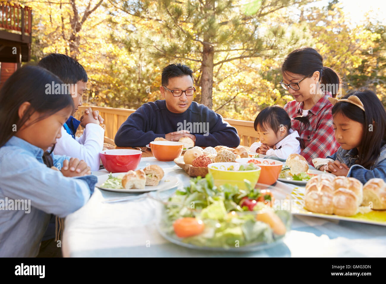 asian-family-at-a-table-on-a-deck-say-a-prayer-before-eating-stock