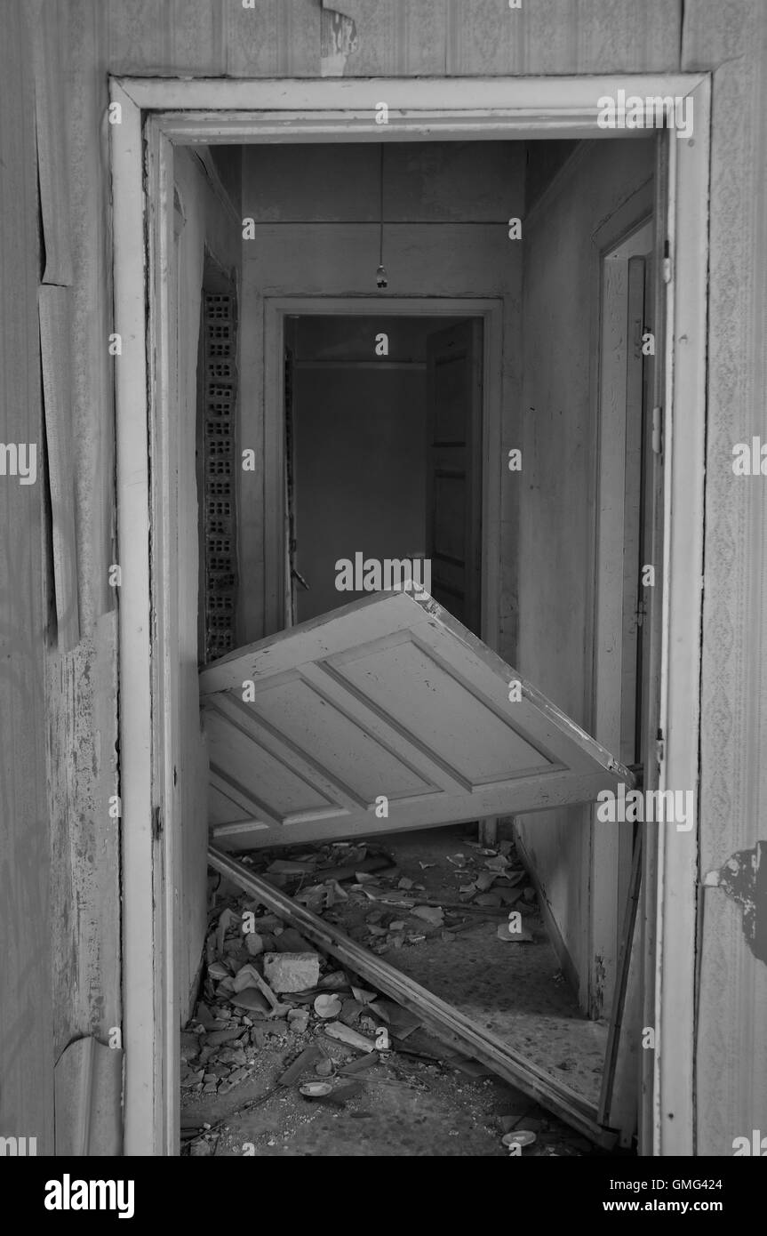 Abandoned house hallway with unhinged door and rubble on dirty floor. Black and white Stock