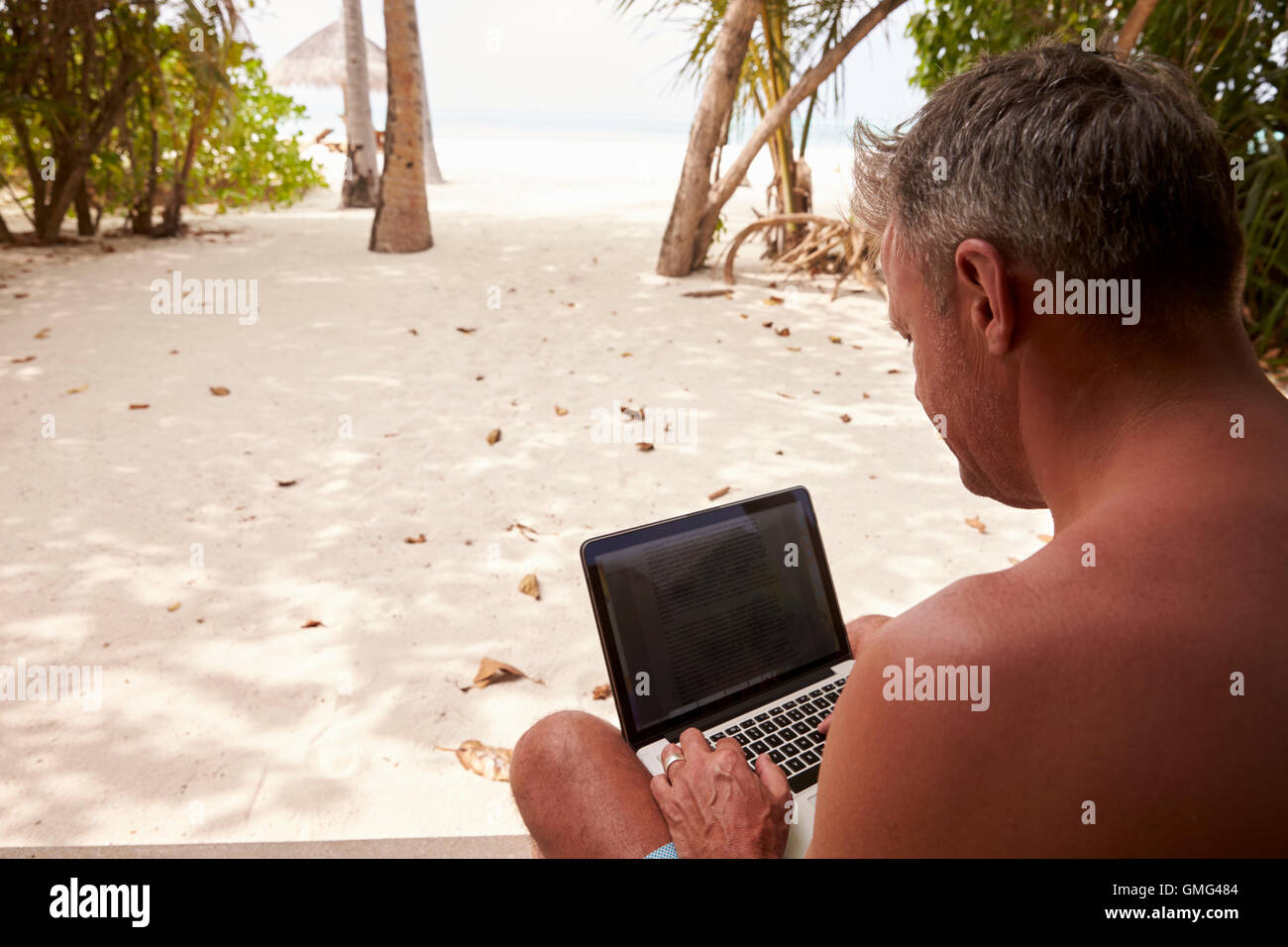 Man using a laptop computer on a beach, over shoulder view Stock Photo ...
