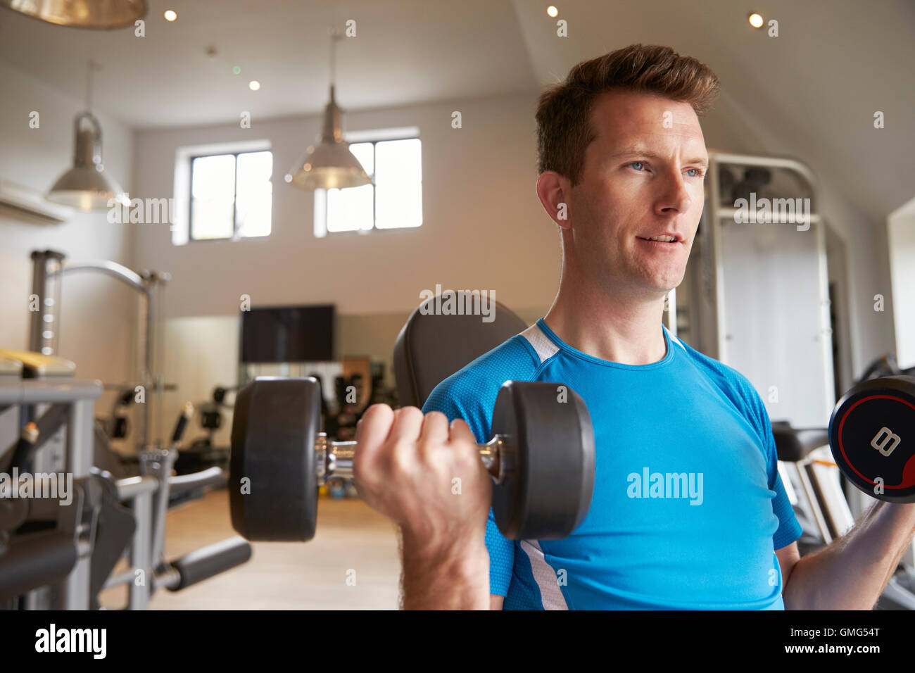 Man practicing bicep curls with dumbbells at a gym, close up Stock Photo