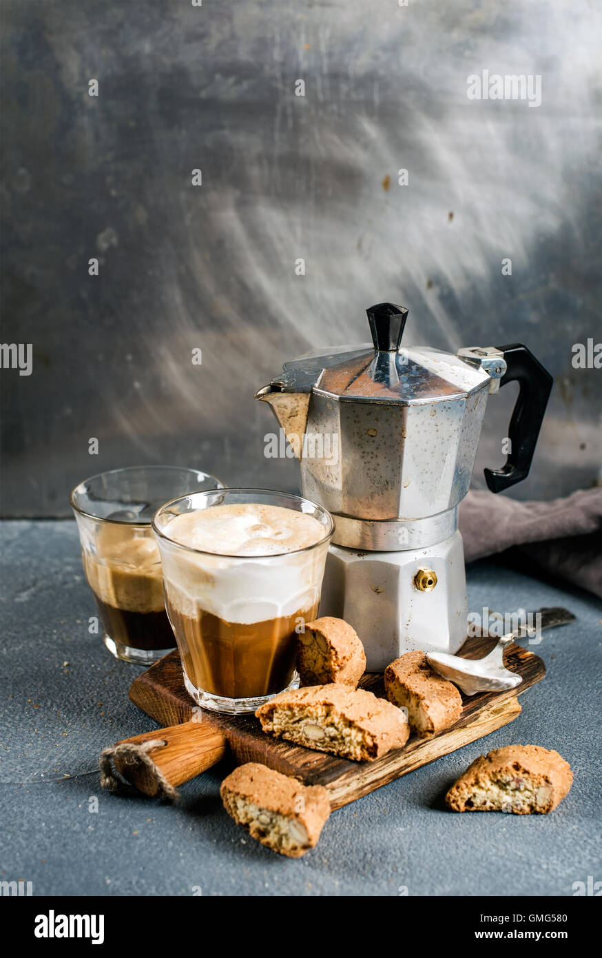 Glass of latte coffee on rustic wooden board, cantucci biscuits and steel Italian Moka pot, grey background Stock Photo