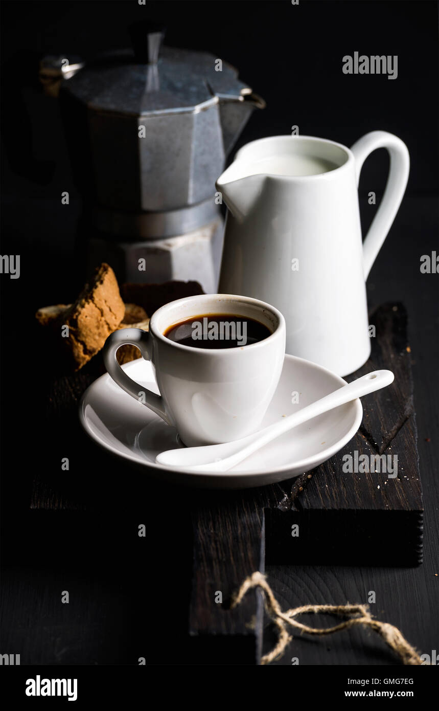Cup of hot espresso, creamer with milk, cantucci and moka coffee pot on