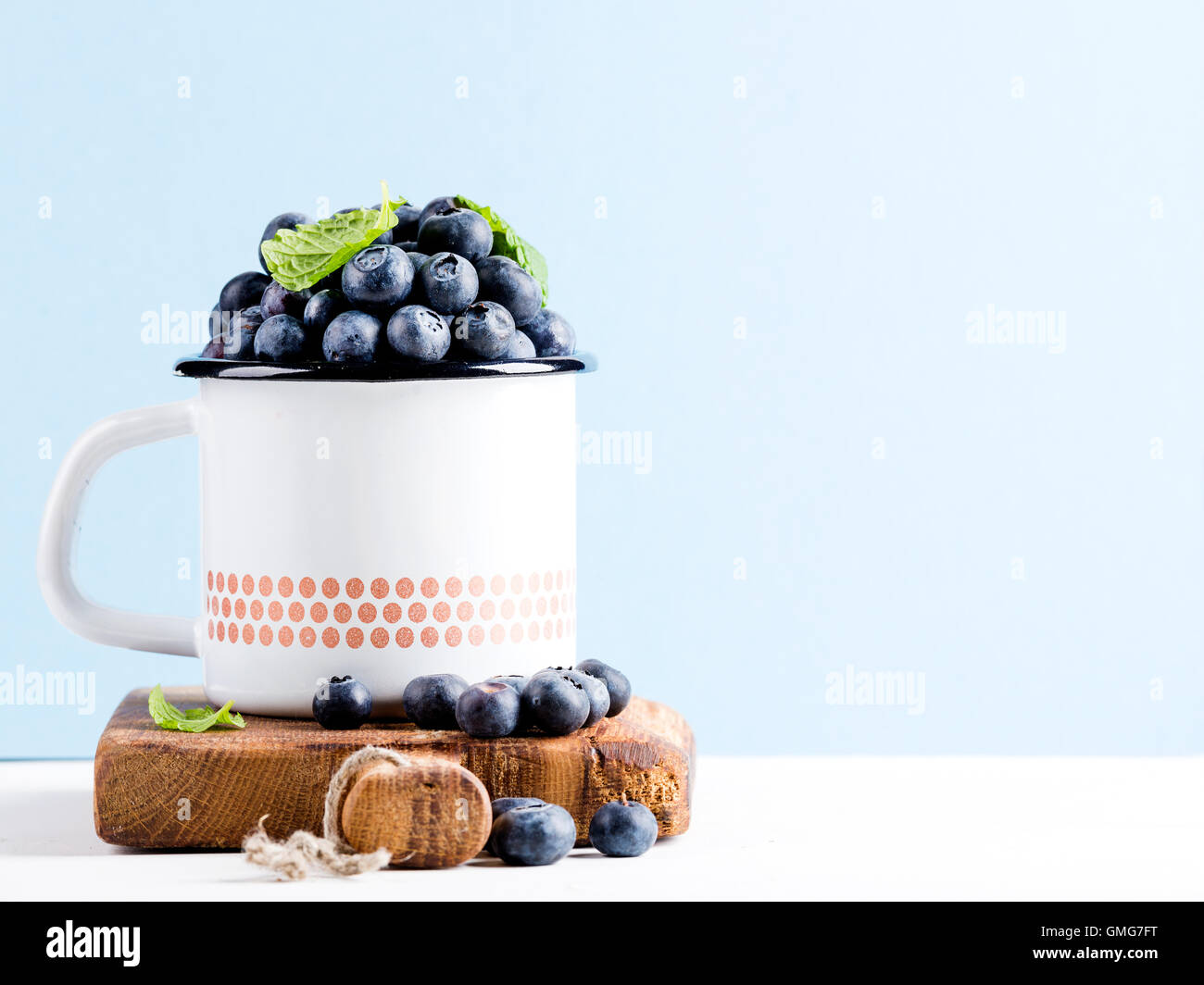 Fresh ripe blueberries in country style enamel mug on rustic wooden board over blue pastel background Stock Photo