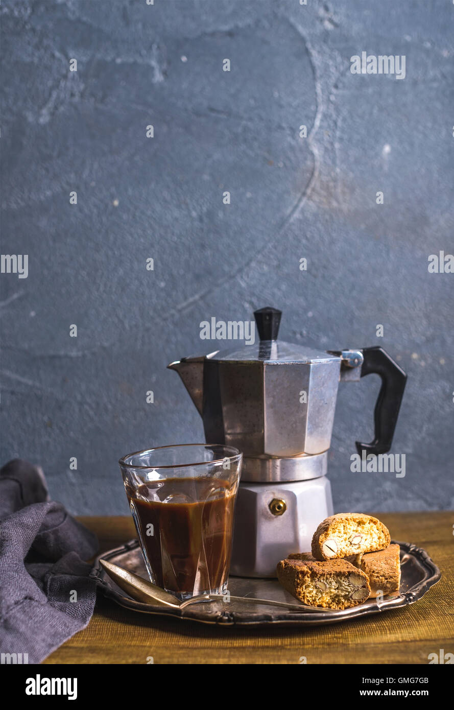 Glass espresso coffee on rustic wooden board, cantucci biscuits and steel Italian Moka pot, grey background Stock Photo