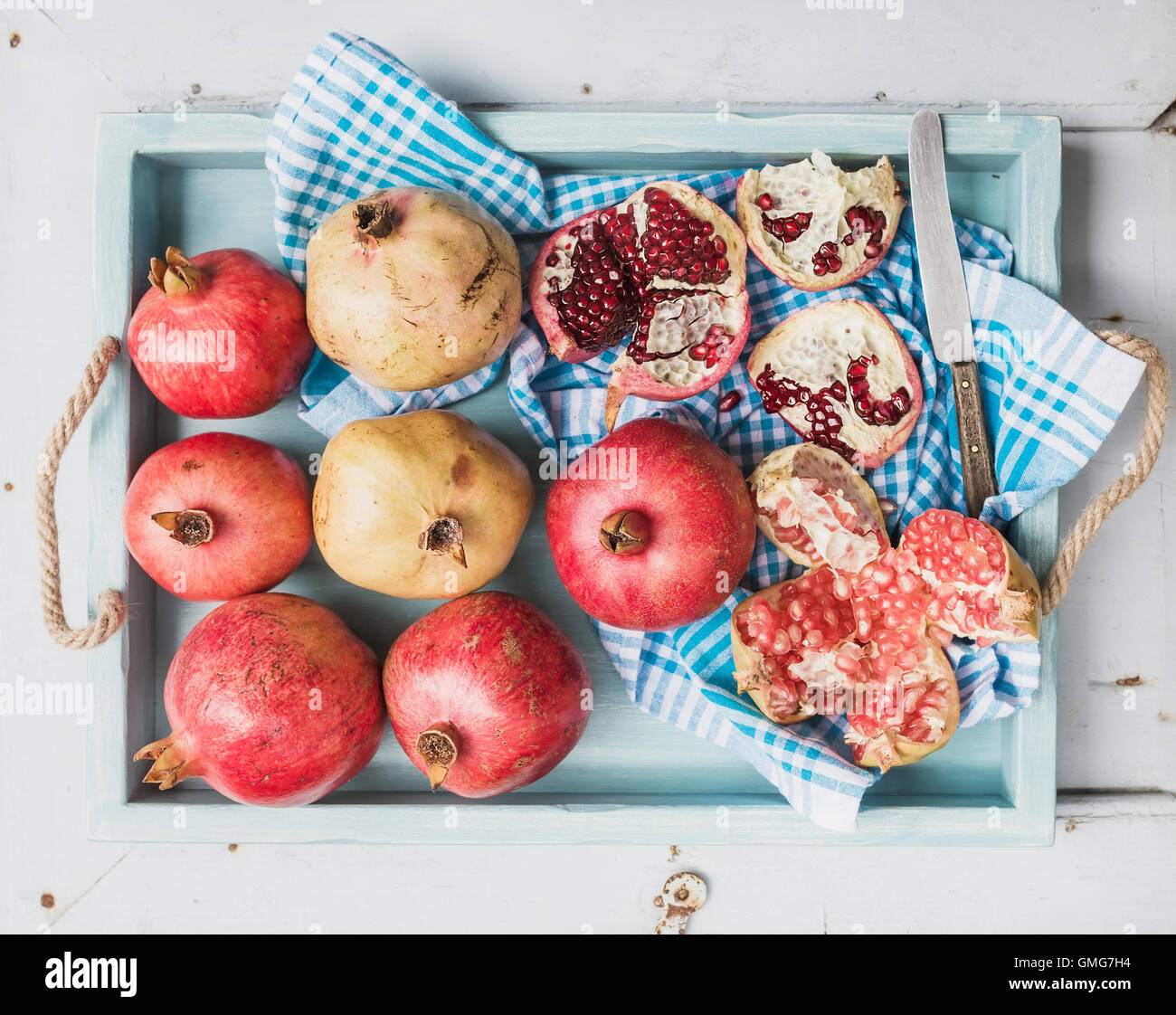 Red and white pomegranates with knife on kitchen towel in blue tray over light painted wooden backdrop Stock Photo