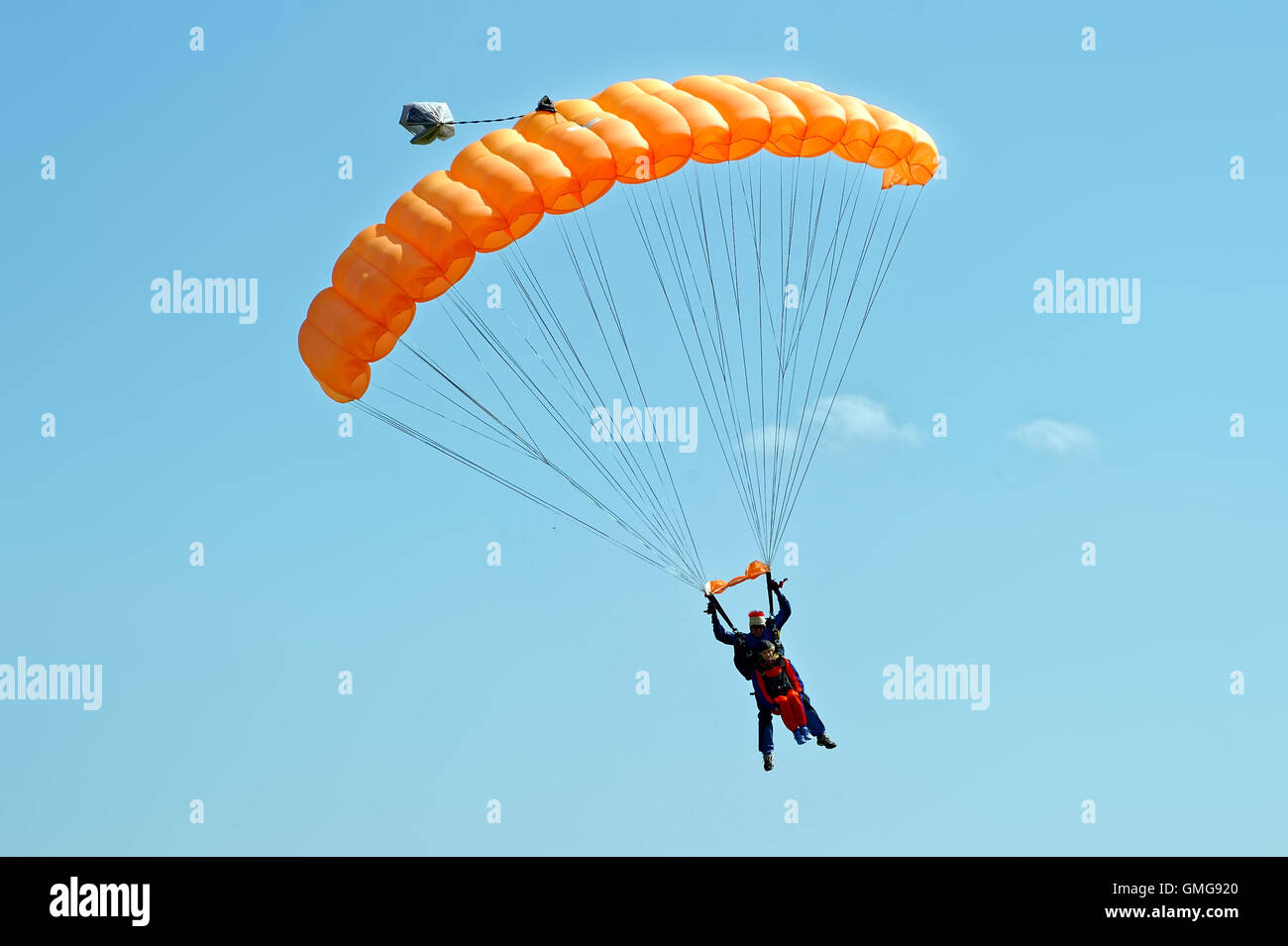 Paraglider flying on orange-colored parachute in blue clear sky at a bright sunny summer day. Active lifestyle, extreme hobbies Stock Photo