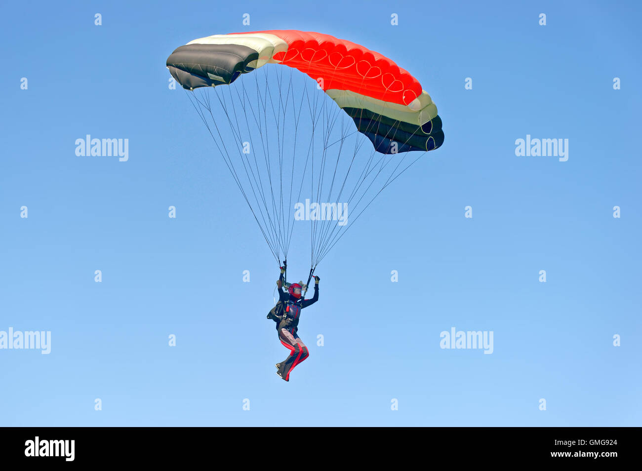 Paraglider flying on colorful parachute in blue clear sky at a bright sunny summer day. Active lifestyle, extreme hobbies Stock Photo