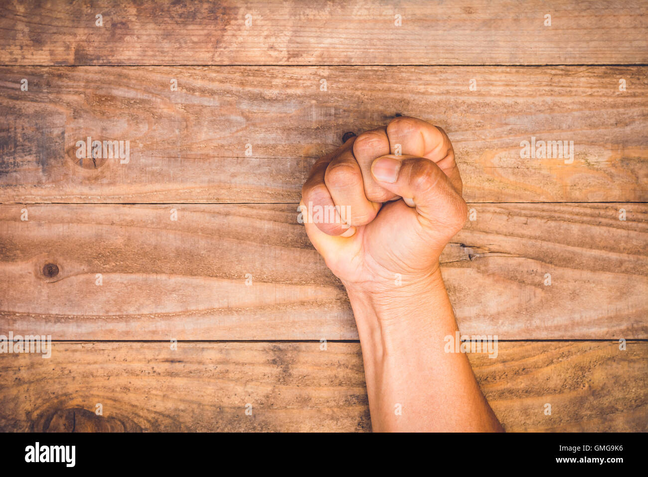 A man fists clenched on a wooden table in anger Stock Photo