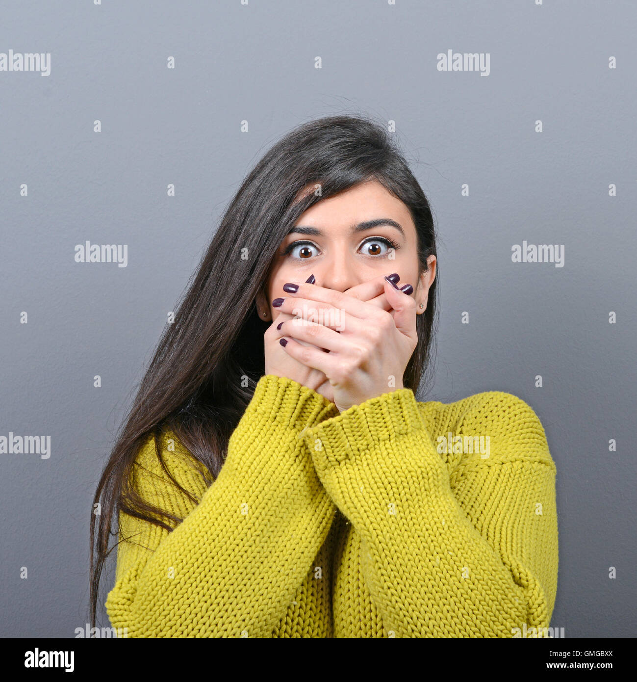 Woman covering her mouth with hands against gray background Stock Photo ...
