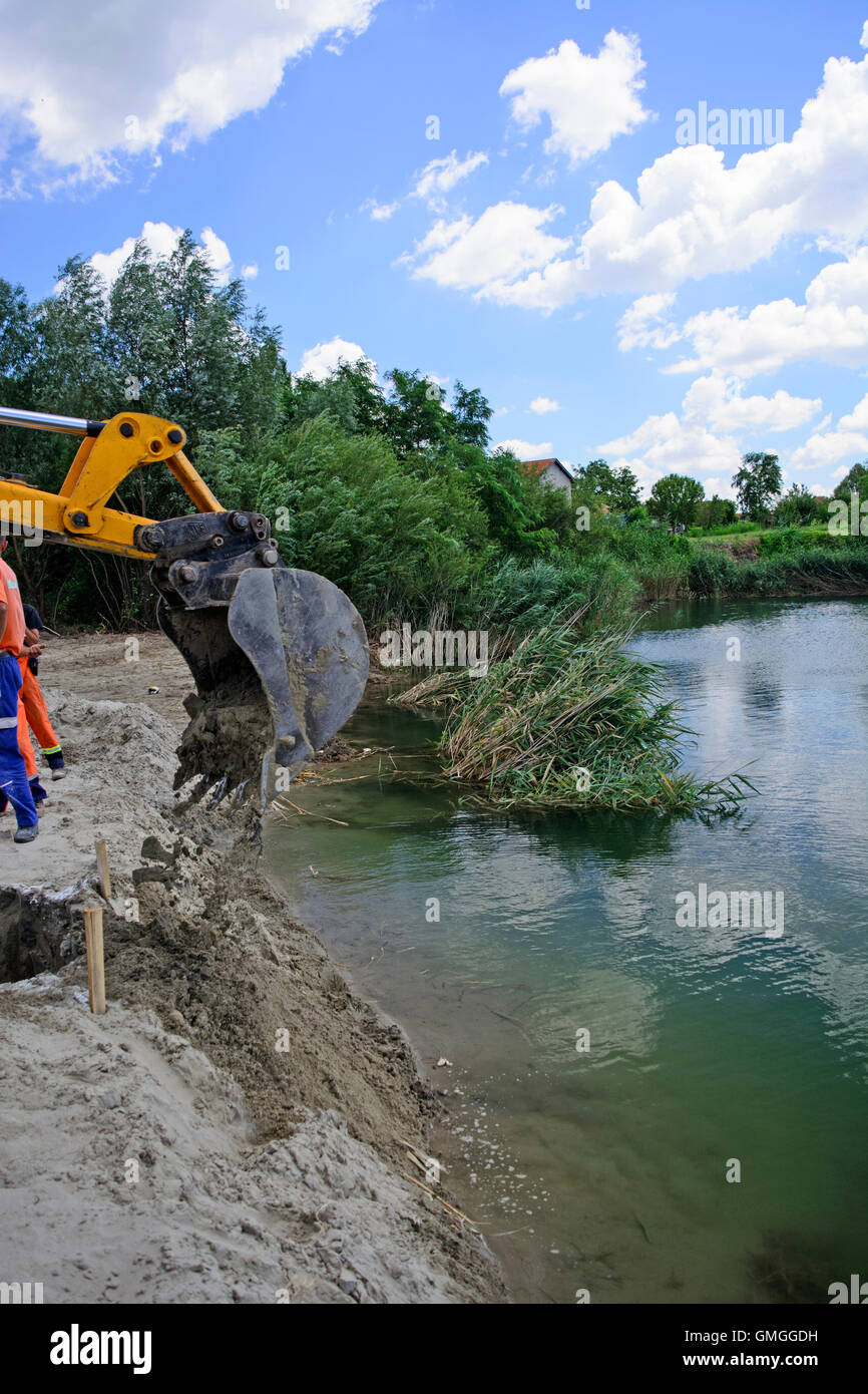 Works that are running a backhoe over water. Stock Photo