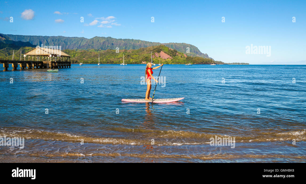 Woman stand up paddling in Hanalei Bay near the Hanalei Pier Stock Photo