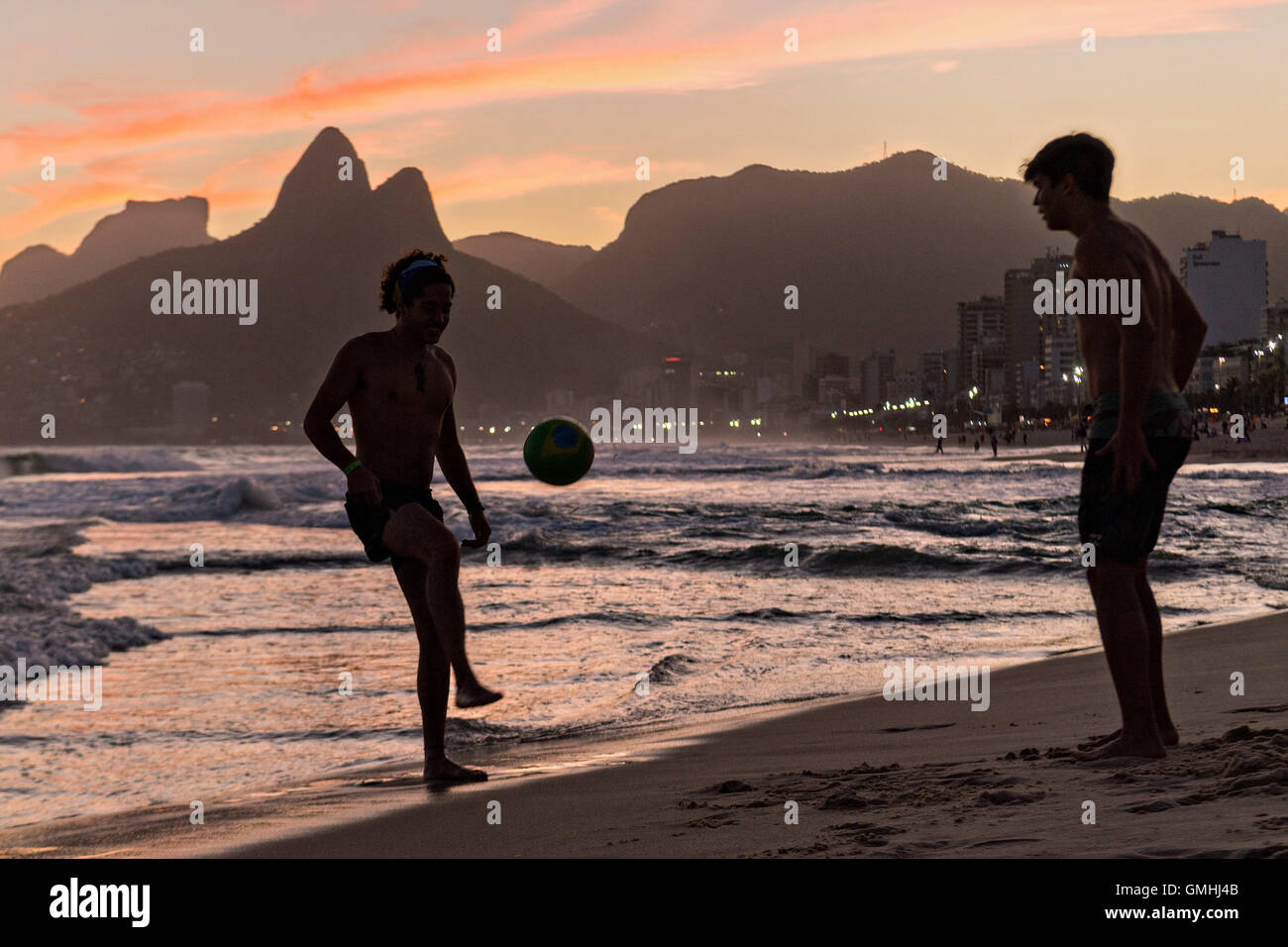 Young men play football on Ipanema beach silhouetted by sunset with the Two Brother mountains in the distance in Rio de Janeiro, Brazil. Stock Photo