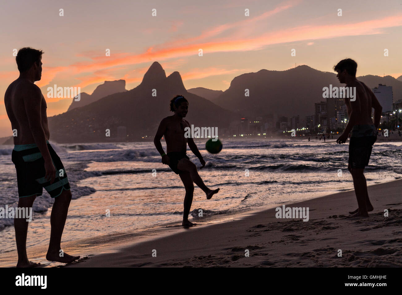 Young men play football on Ipanema beach silhouetted by sunset with the Two Brother mountains in the distance in Rio de Janeiro, Brazil. Stock Photo