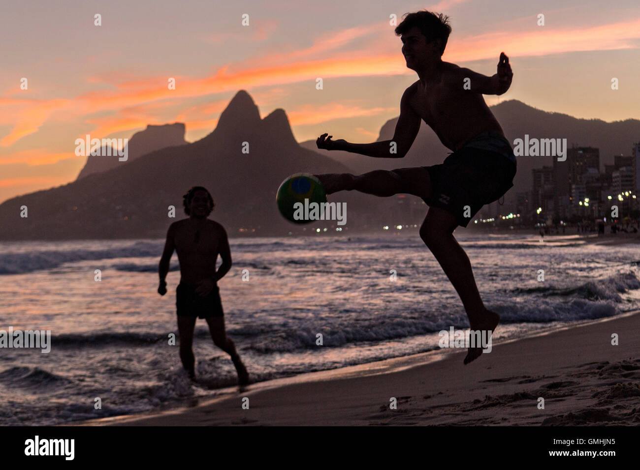 Young men play football on Ipanema beach silhouetted by sunset with the Two Brother mountains in the distance in Rio de Janeiro, Brazil. Stock Photo