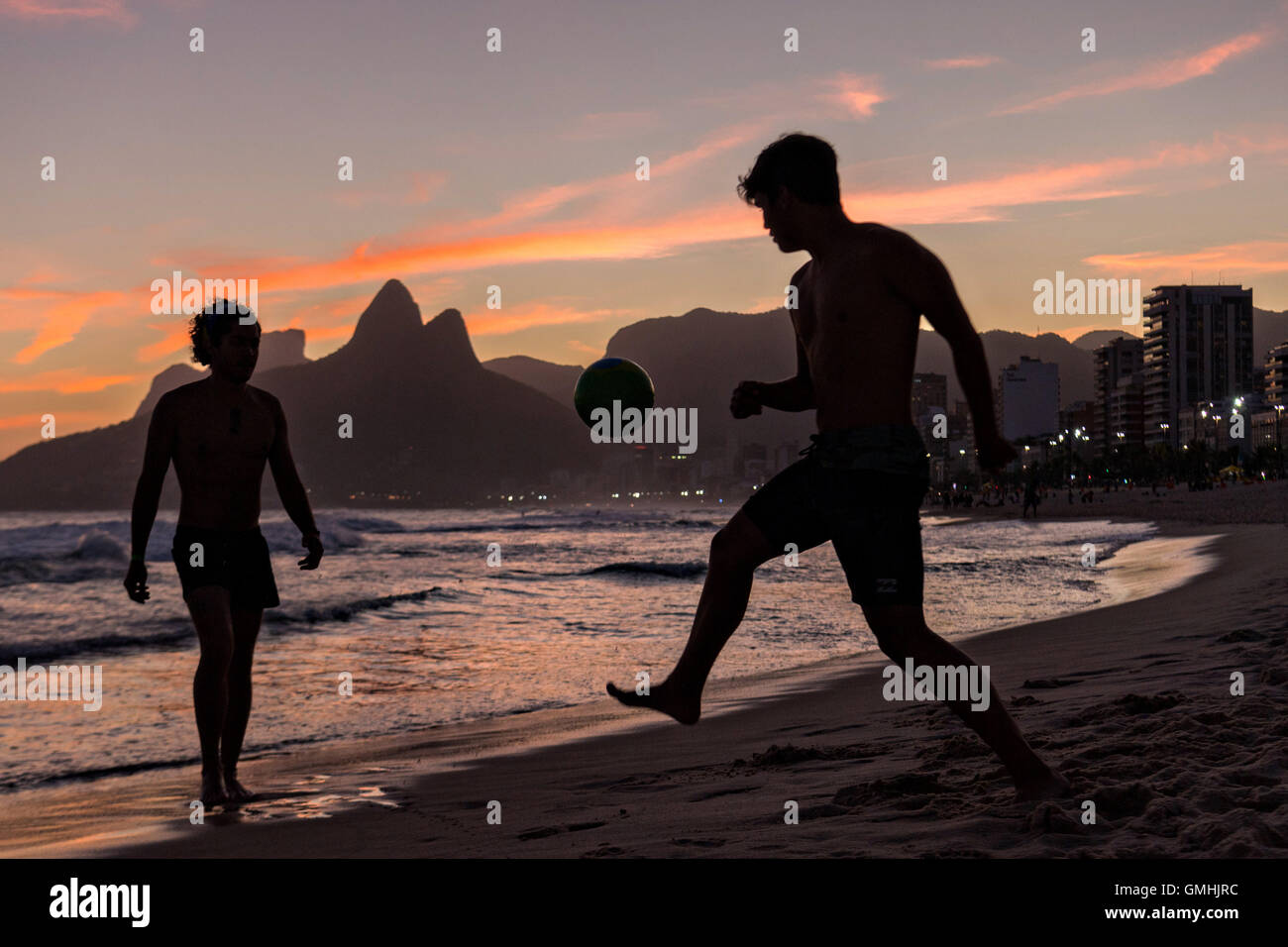 Young men play football on Ipanema beach silhouetted by sunset with the Two Brother mountains in the distance in Rio de Janeiro, Brazil. Stock Photo