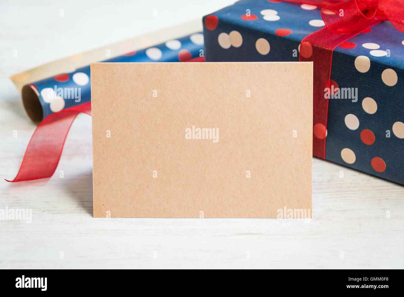 Empty greeting kraft card. Wrapped gift and wrapping materials over a white wood background. Stock Photo
