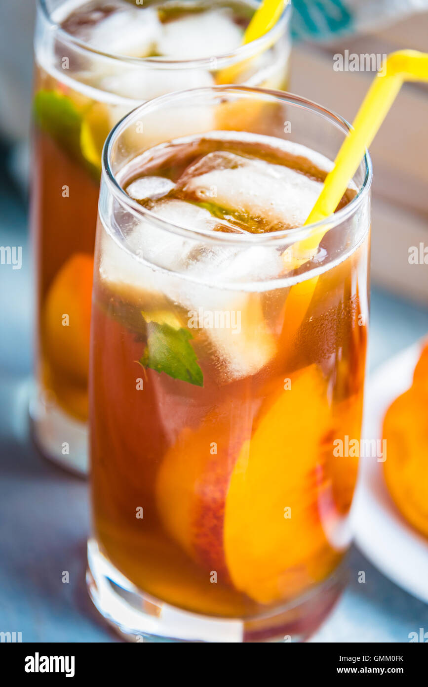 Glasses with homemade ice tea, peach flavored. Freshly cut peach slices for arrangement. Light blue wood background. Stock Photo