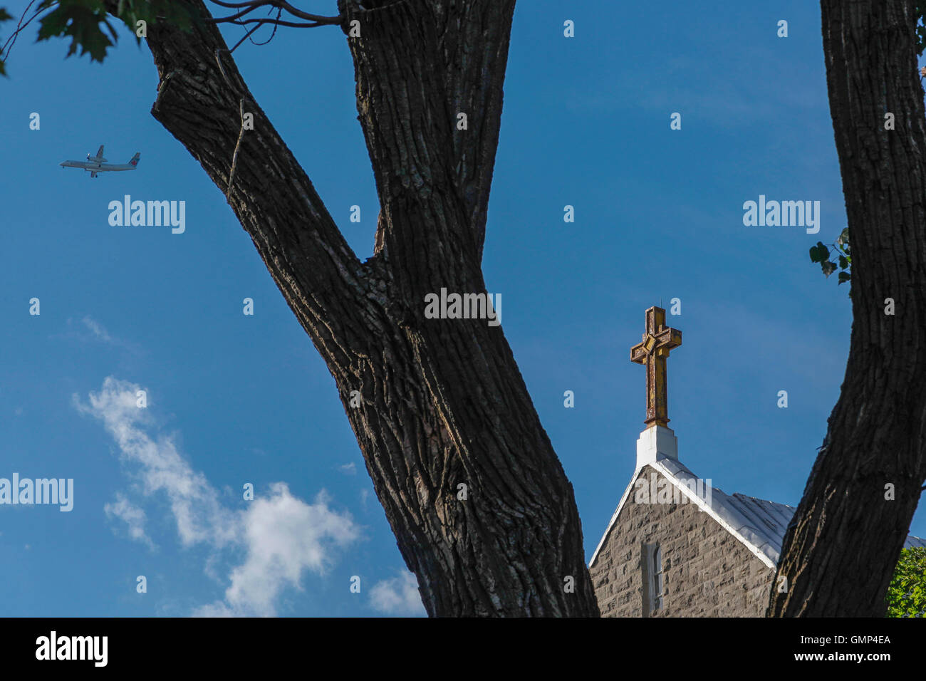 A church cross framed between tree trunks with an aircraft passing by. Stock Photo