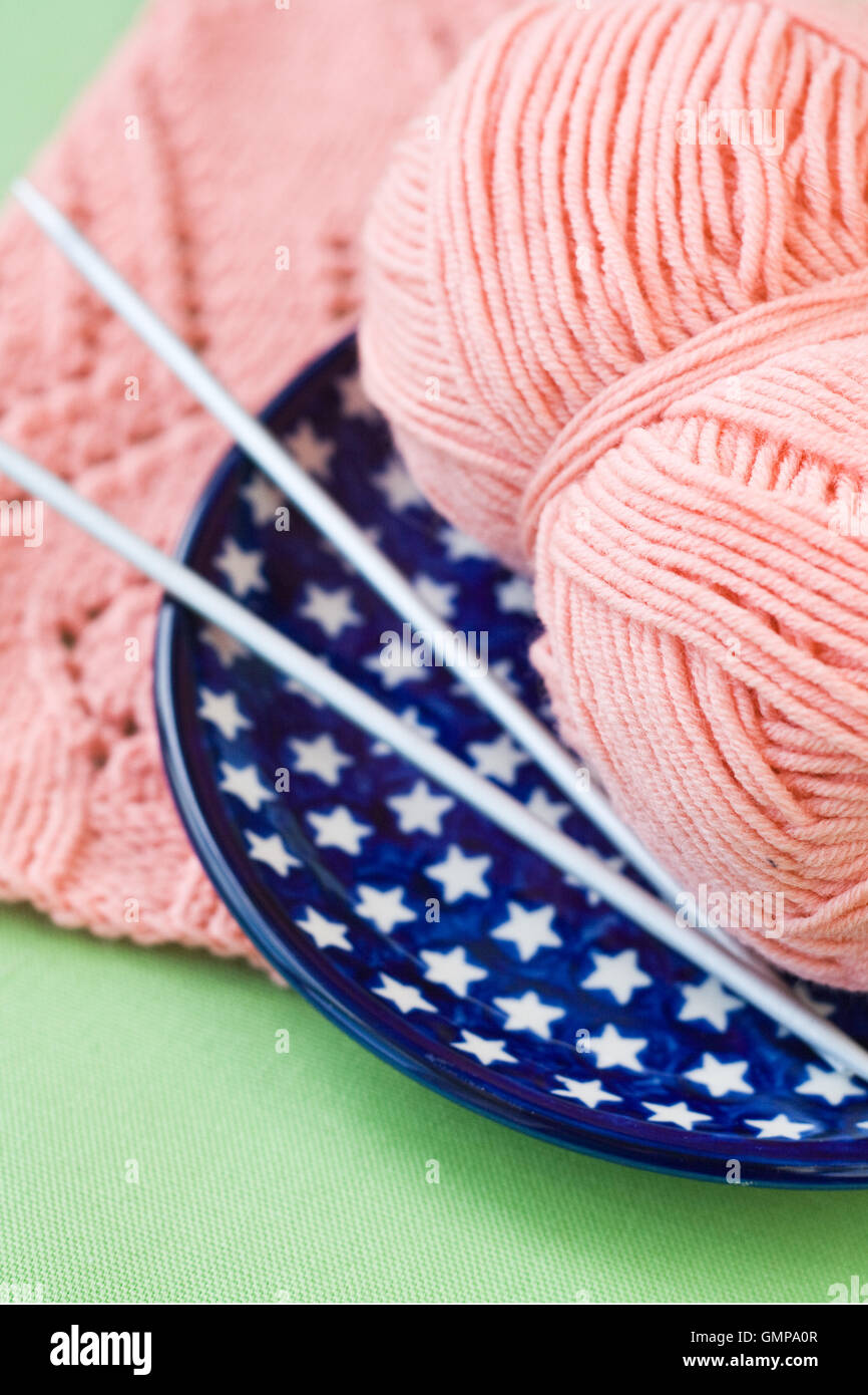 A ball of pink yarn and knitting needles on a blue plate Stock Photo