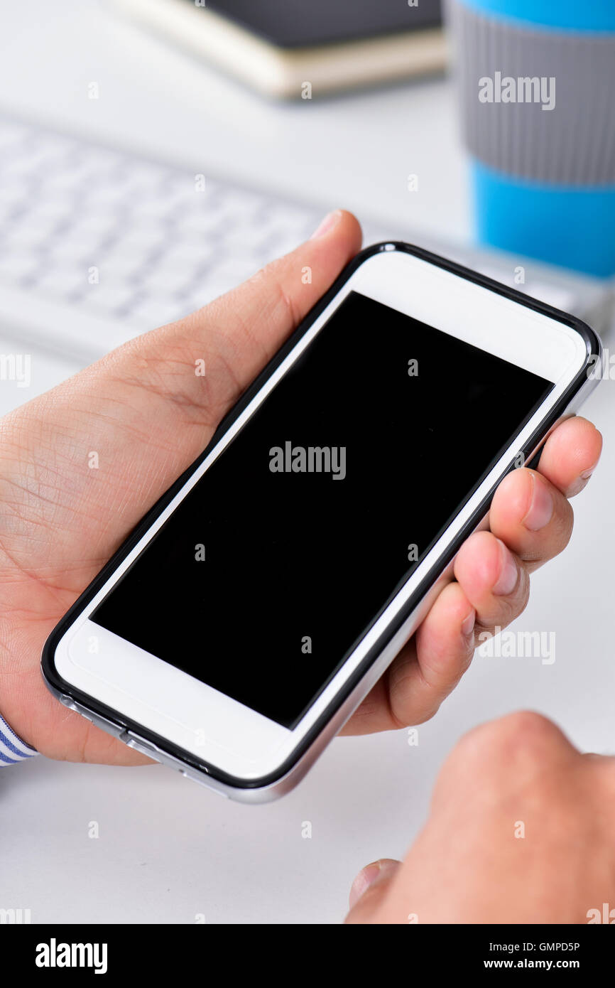 closeup of a businessman sitting at his office desk, with his smartphone in his hand with a black blank space in its screen Stock Photo