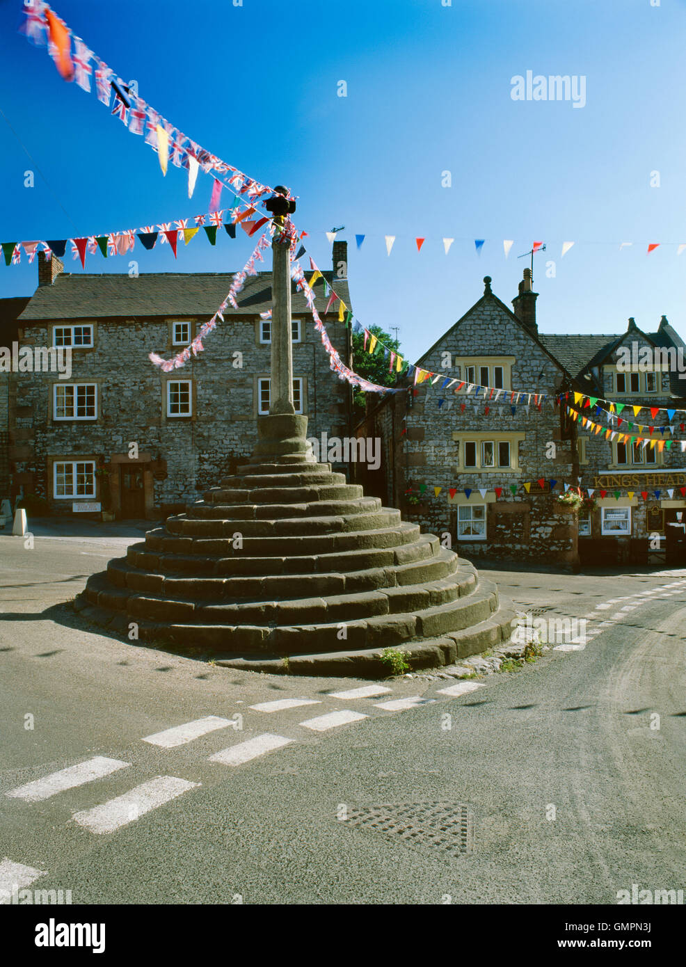 Bonsall, Derbyshire: Medieval Market Cross, and King's Head pub, decorated with bunting for the village well dressings in August. Stock Photo