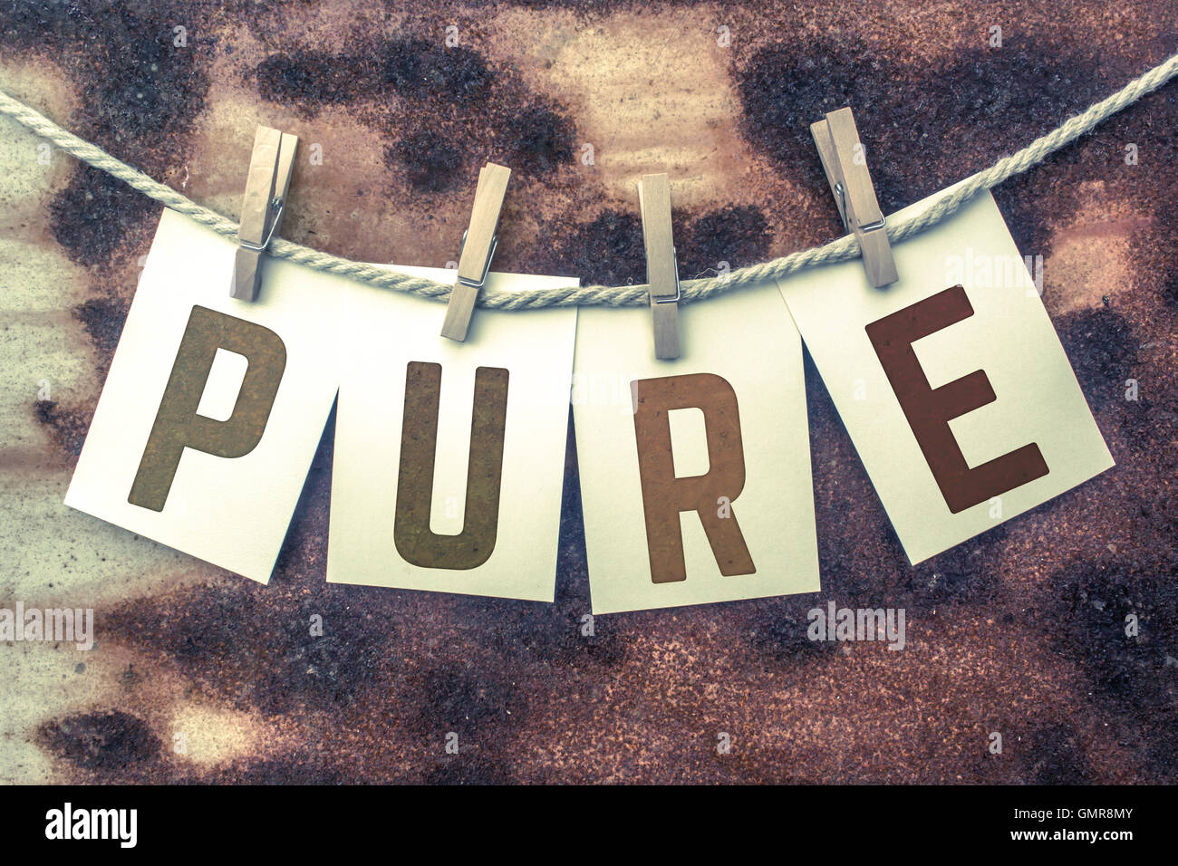 The word 'PURE' stamped on cards and pinned to an old piece of twine over a rusted metal background. Stock Photo