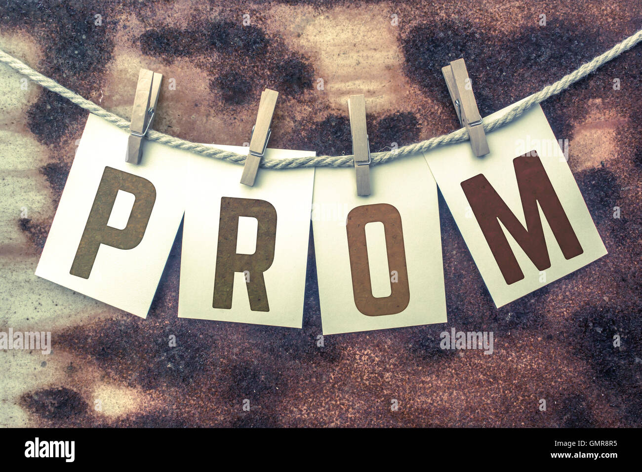 The word 'PROM' stamped on cards and pinned to an old piece of twine over a rusted metal background. Stock Photo
