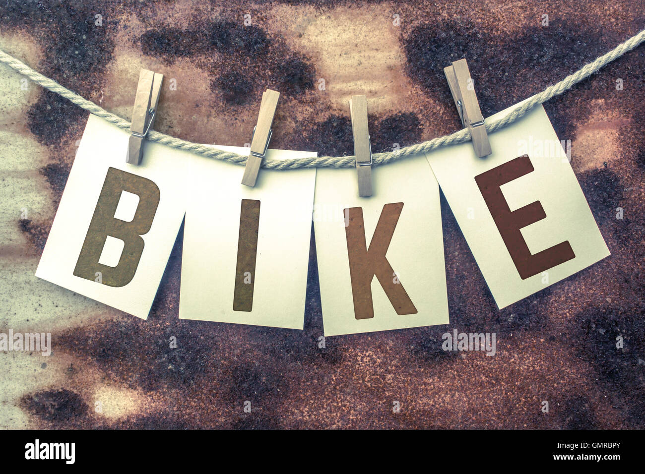 The Word BIKE Stamped On Cards And Pinned To An Old Piece Of Twine Over A Rusted Metal 