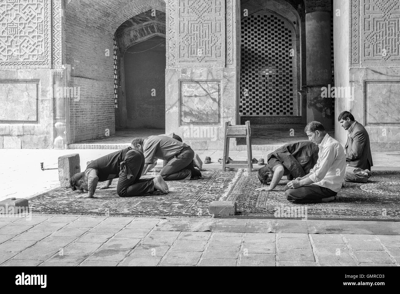 The Jāmeh Mosque of Isfahān is the grand, congregational mosque (Jāmeh) of Isfahān, Iran.  Men kneel for noon prayers. Monochrome. Stock Photo