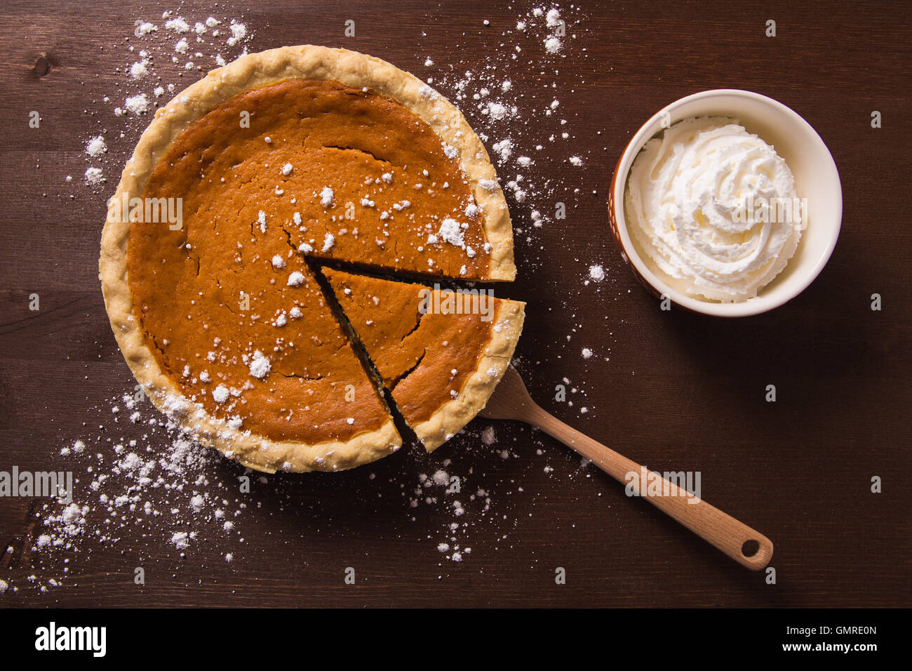 An overhead view of a gourmet pumpkin pie with a side of whipped cream on a rustic wood table surface Stock Photo