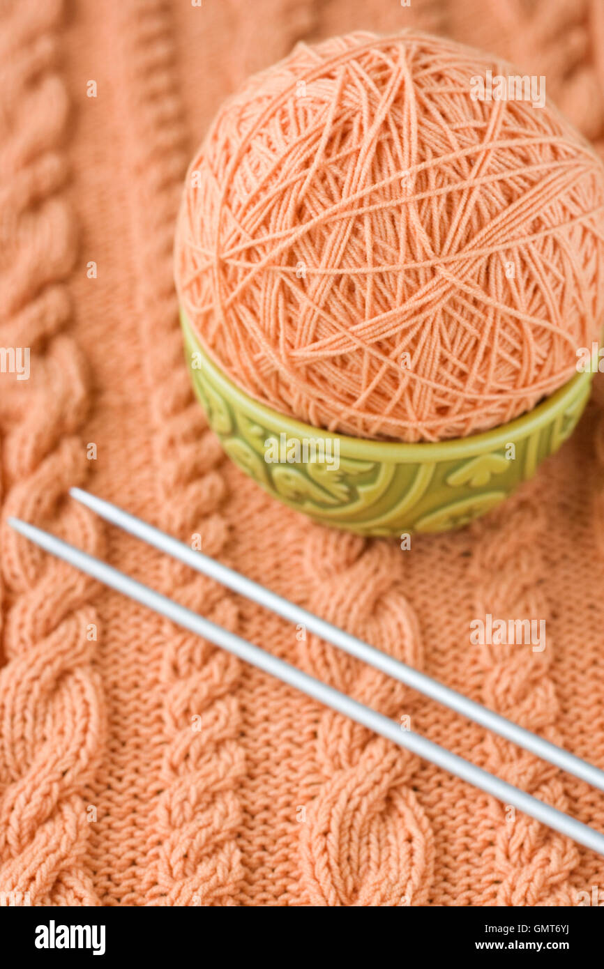 A peachcolored ball of yarn are in the national dish and needles for