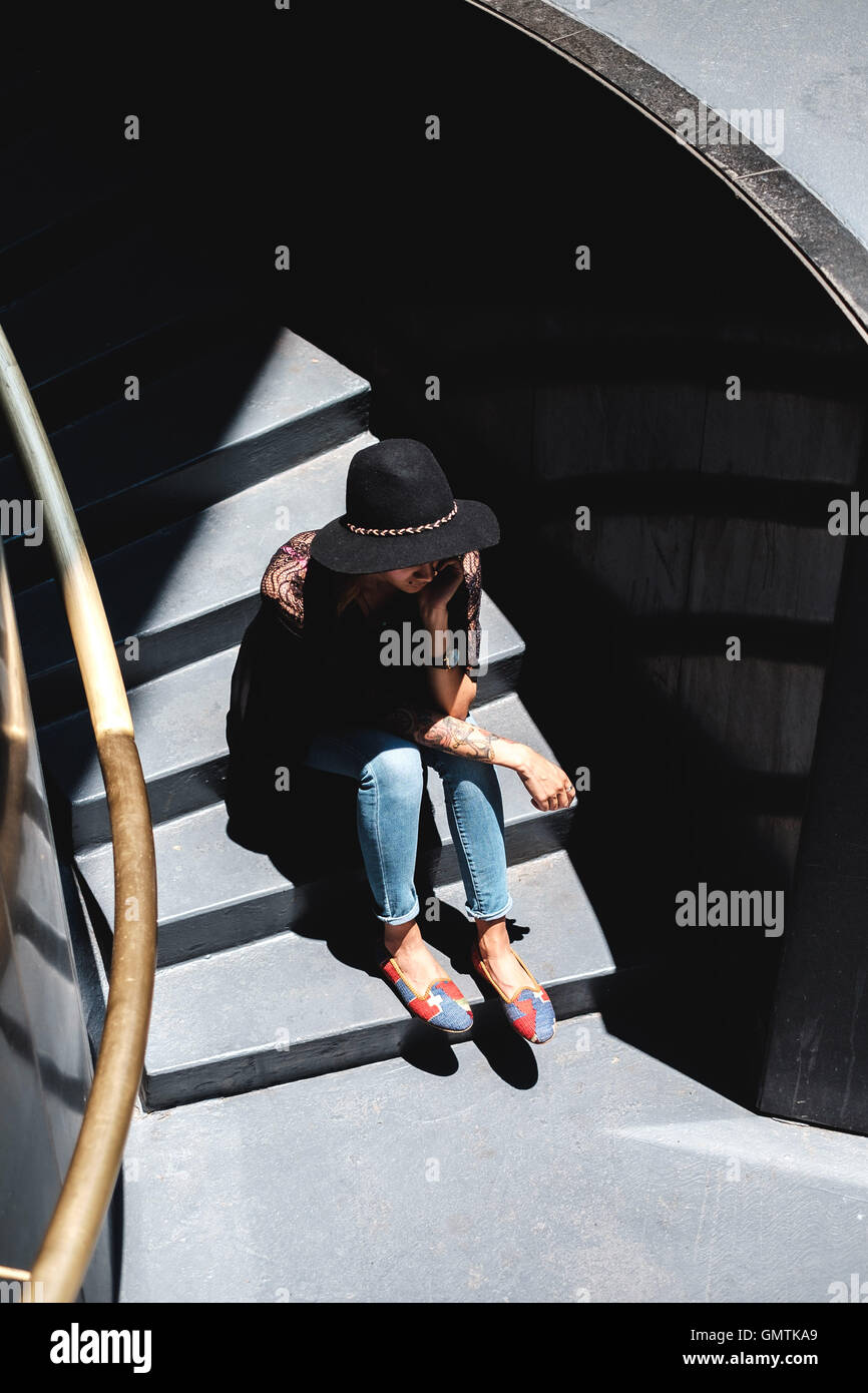 Girl with tattoos in stylish clothes and hat sitting in down on steps Stock Photo