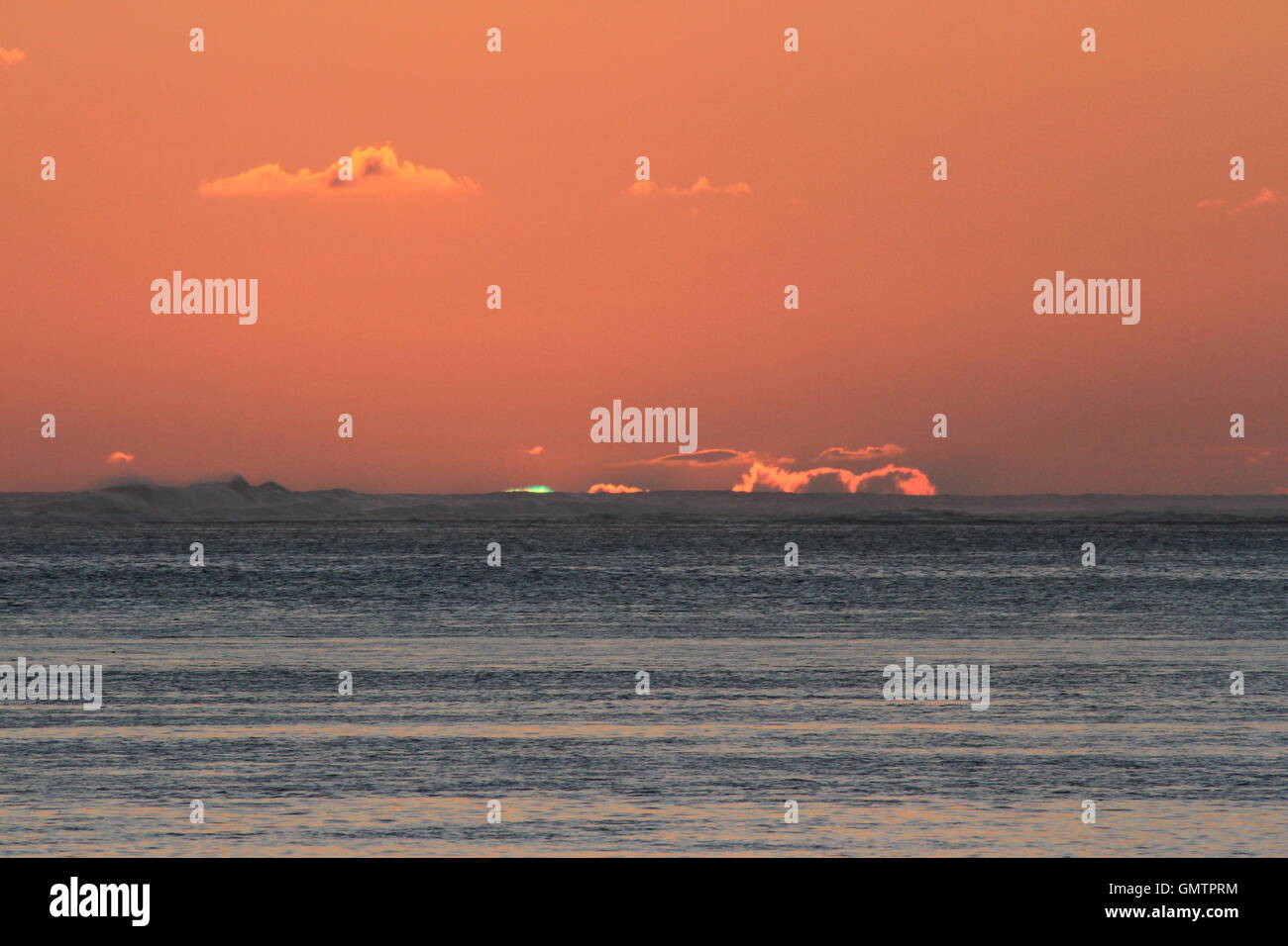 Sunset on Mauritius with a rare green flash visible beyond the waves crashing on the reef Stock Photo