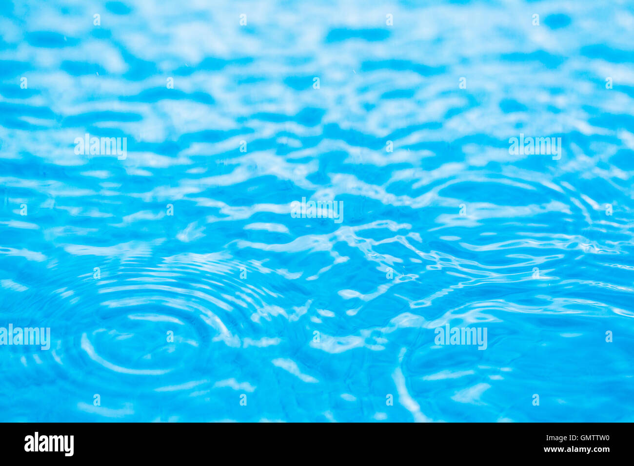 The rings and ripples formed by rain drops on  swimming pool water on a still sunny day, above the swimming pool steps, Stock Photo