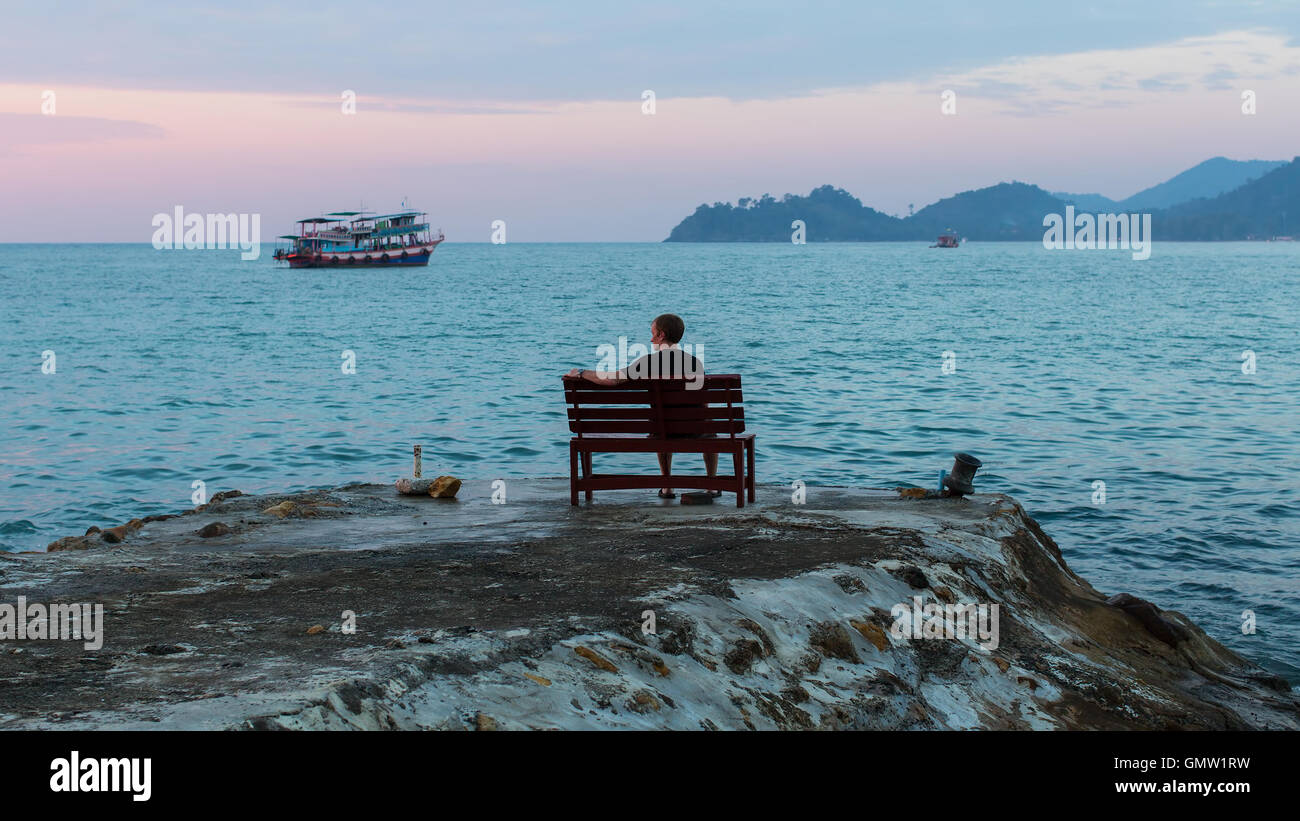 A young man sits alone on a bench on the seafront promenade. Stock Photo