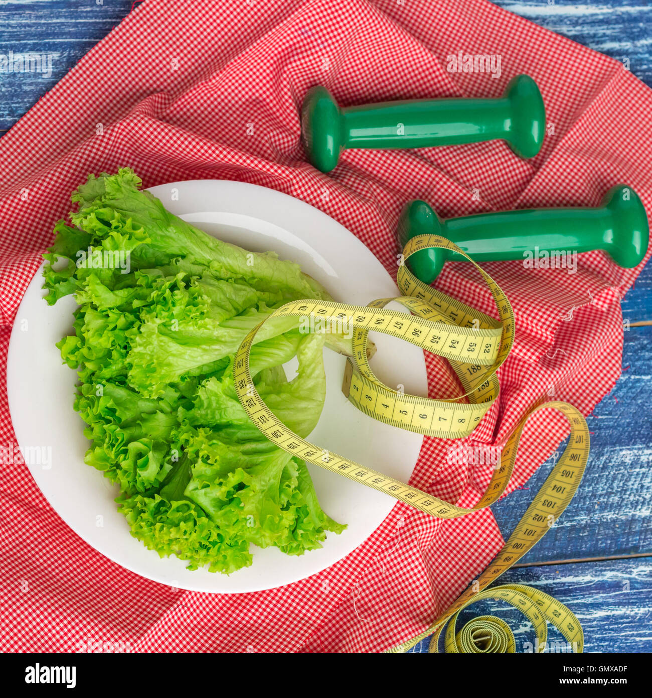 Fitness composition of green lettuce on white plate, weights and ruler Stock Photo