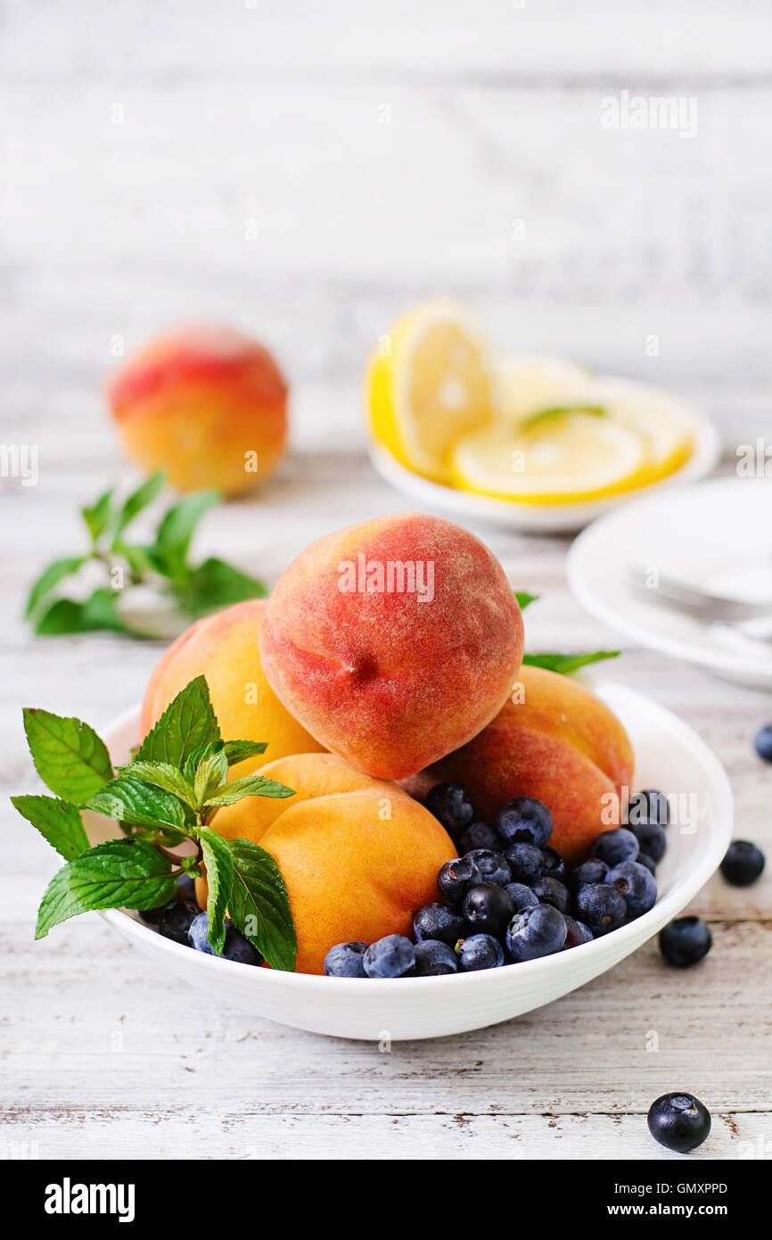 Fresh peaches and blueberries in bowl on a light wooden background in rustic style Stock Photo