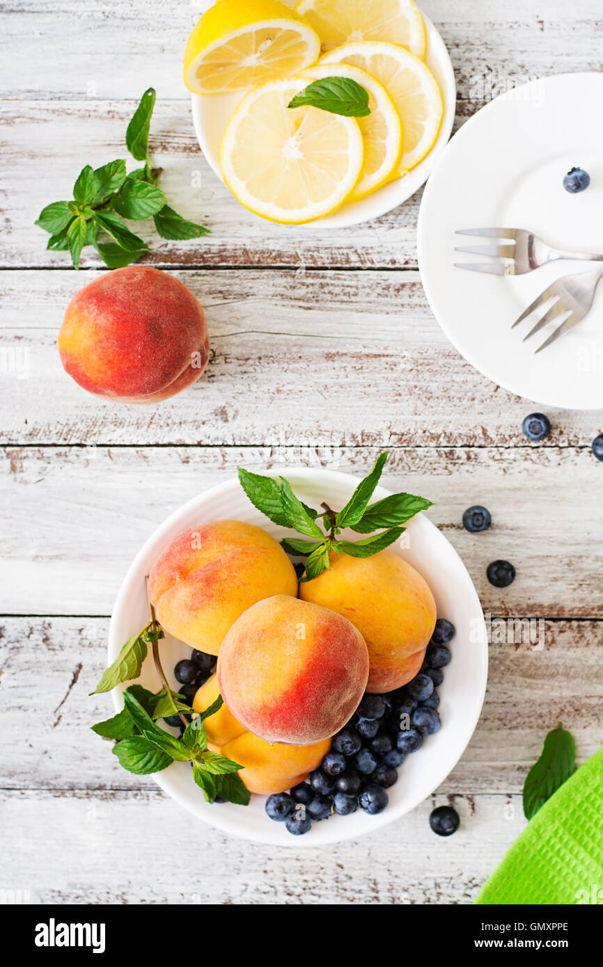 Fresh peaches and blueberries in bowl on a light wooden background in rustic style. Top view Stock Photo