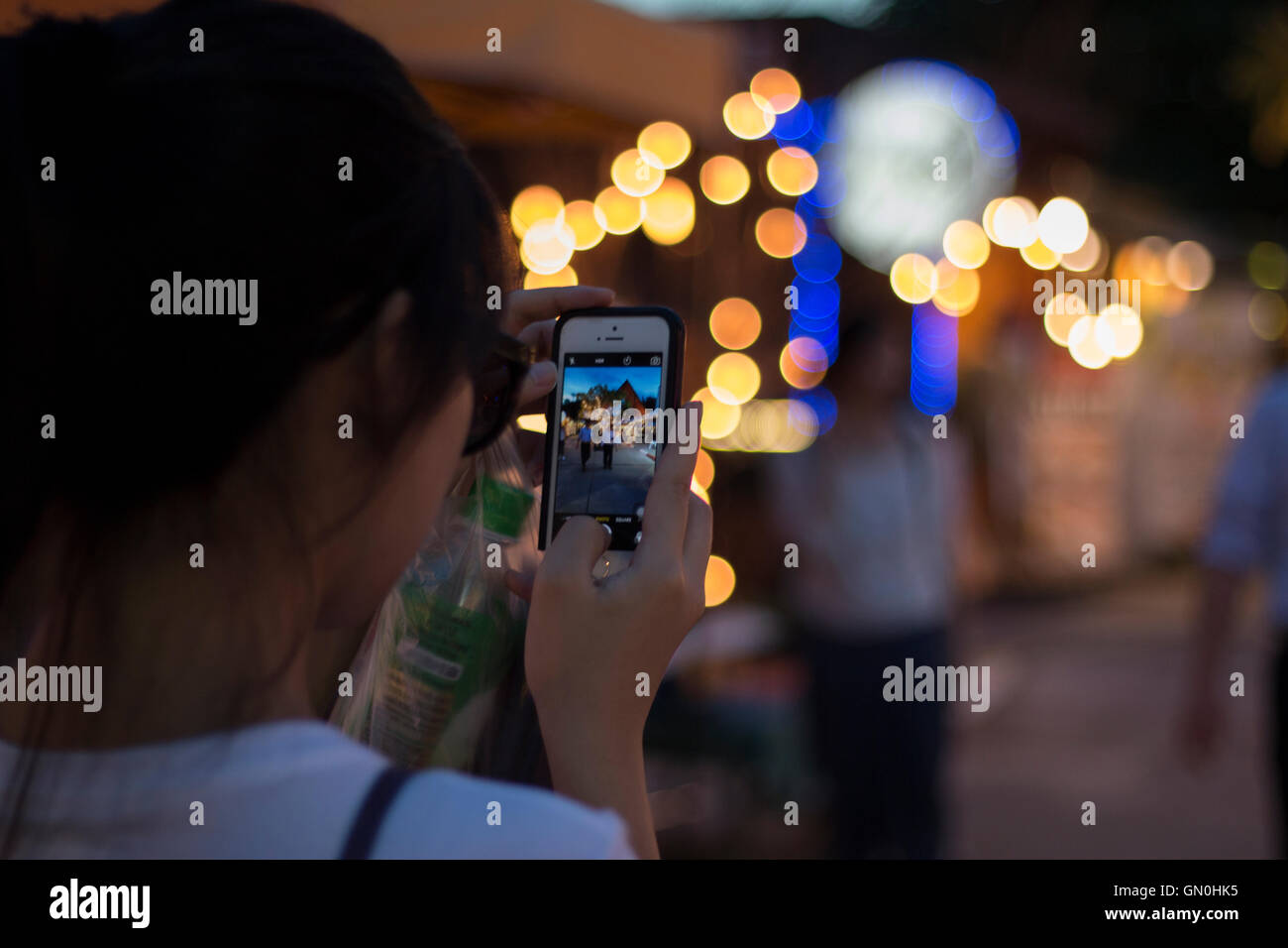 Asian woman taking picture with her cellphone at night Stock Photo