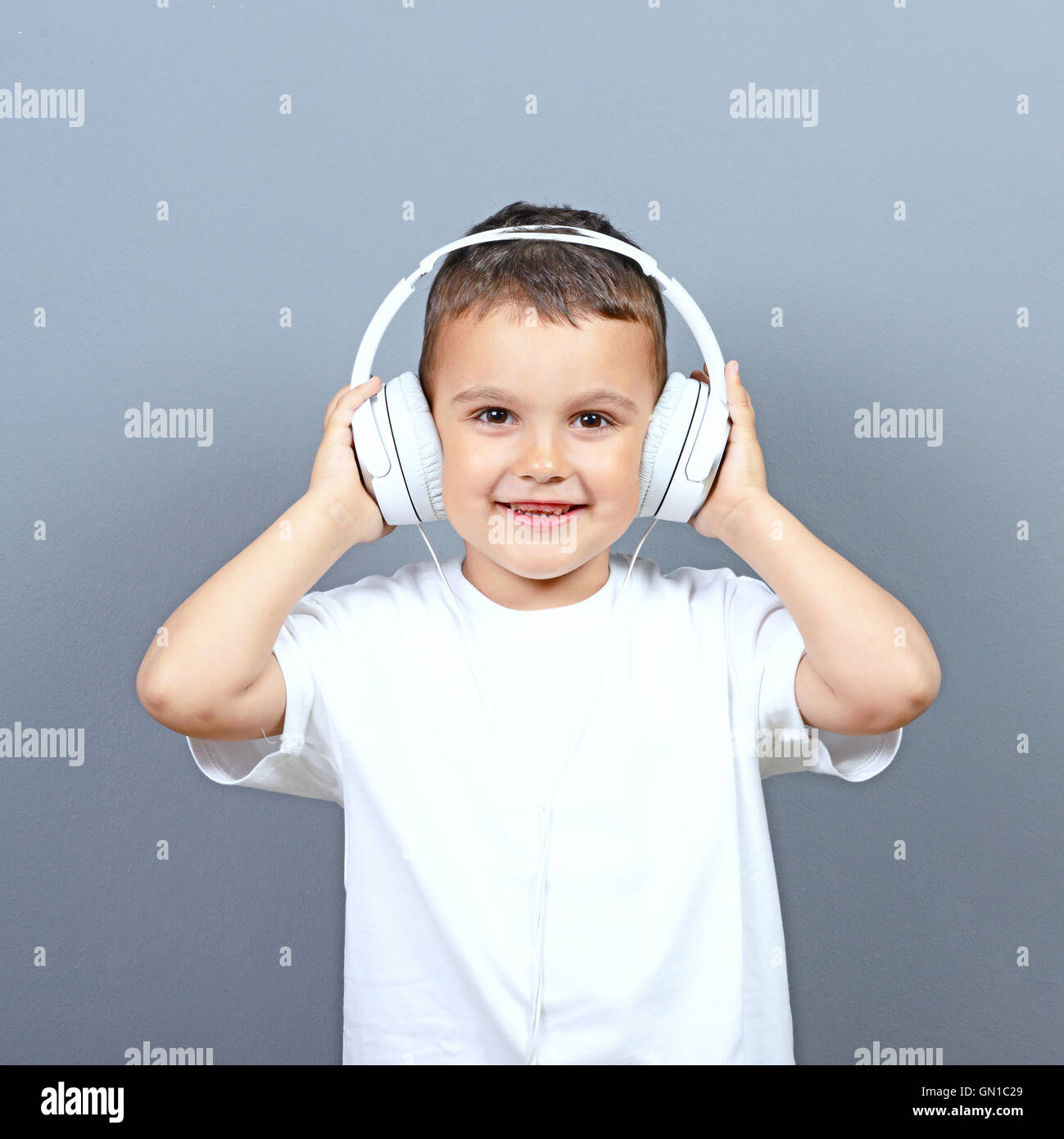 Cute little boy kid listening music on big headphones against gray