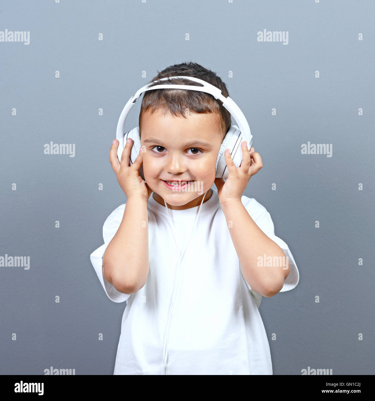 Cute little boy kid listening music on big headphones against gray