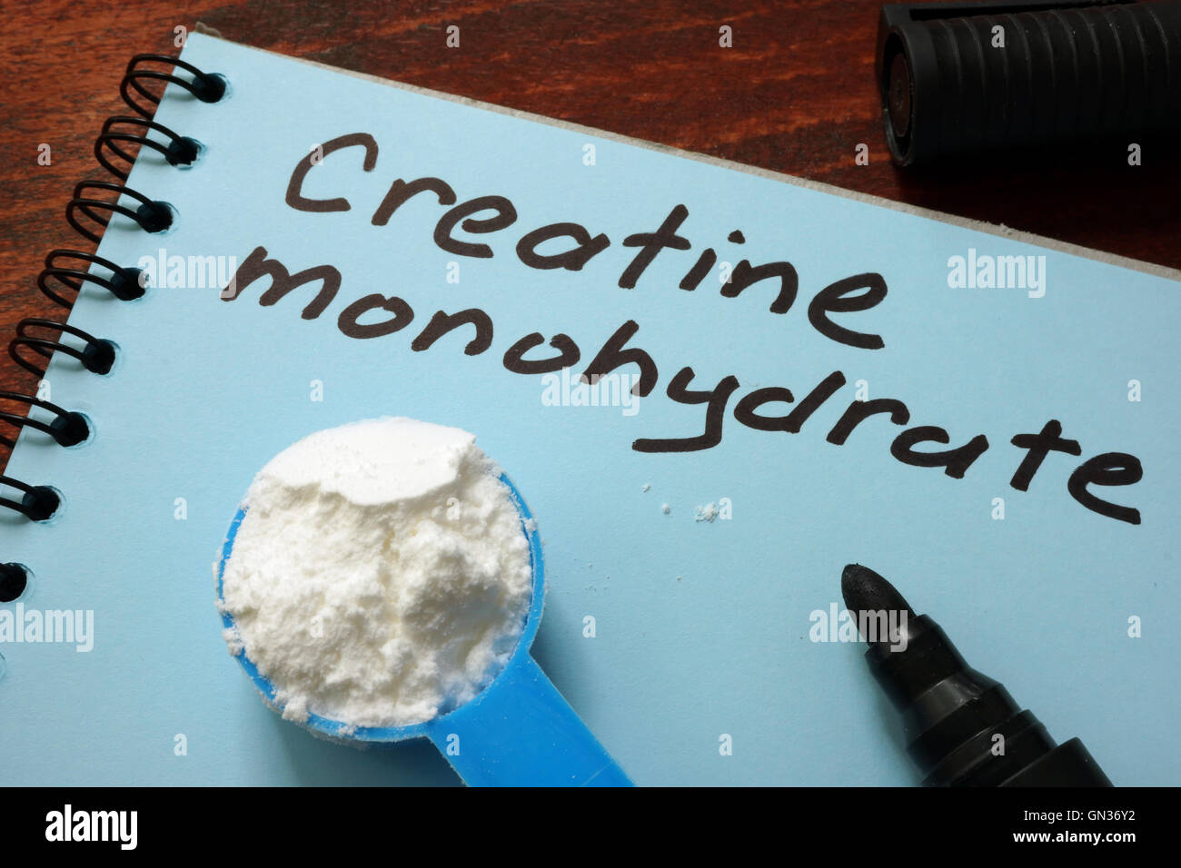 Notebook with  sign Creatine monohydrate and scoop with white powder. Stock Photo