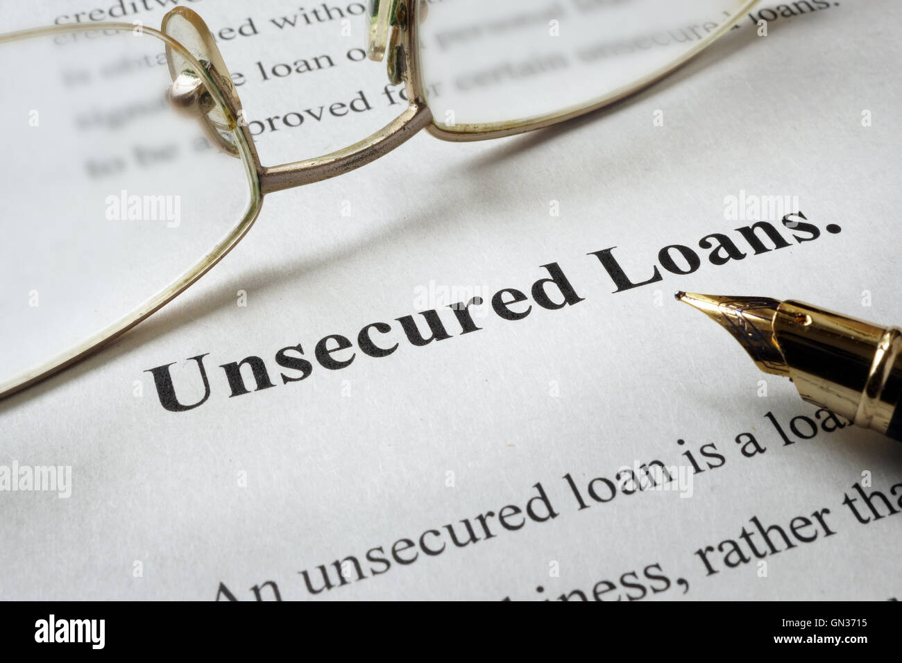 Page of paper with words unsecured loans and glasses. Stock Photo