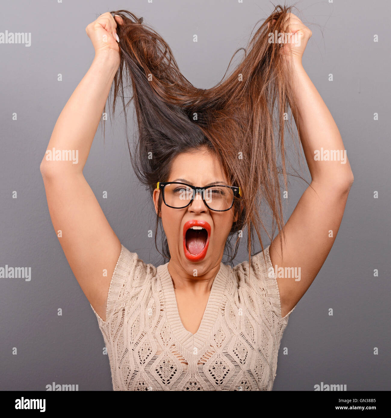 Portrait of a histerical woman pulling hair out against gray background
