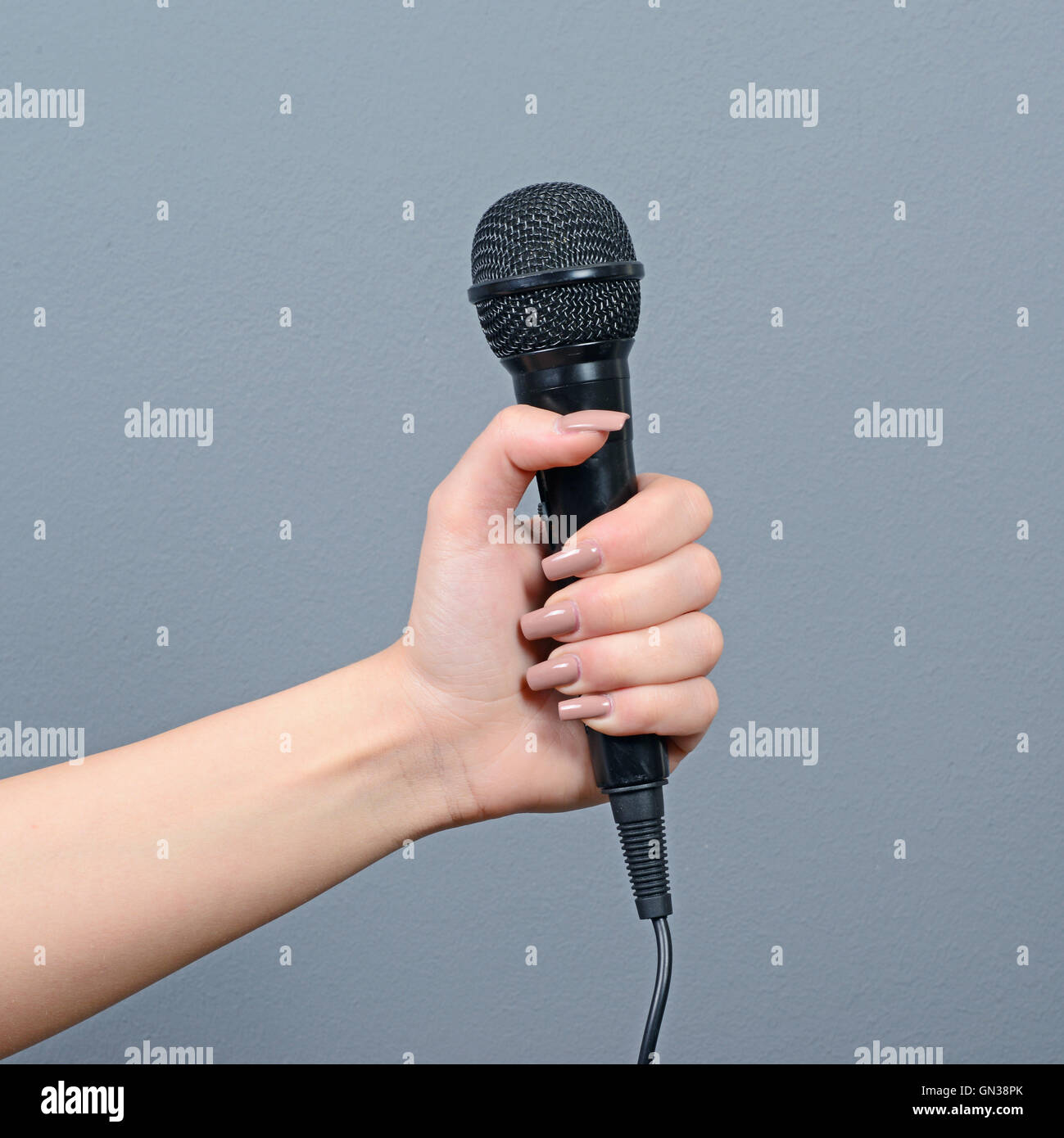 Hand holding microphone against gray background Stock Photo