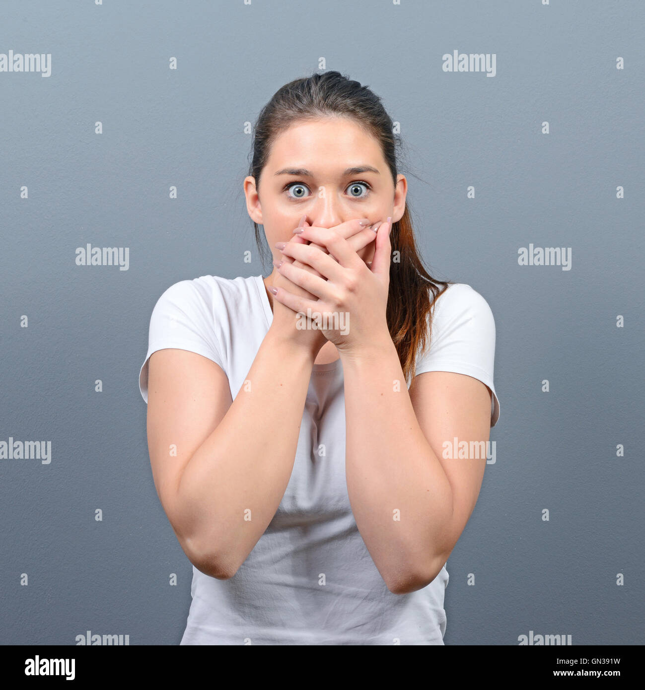 Woman covering her mouth with hands against gray background Stock Photo ...