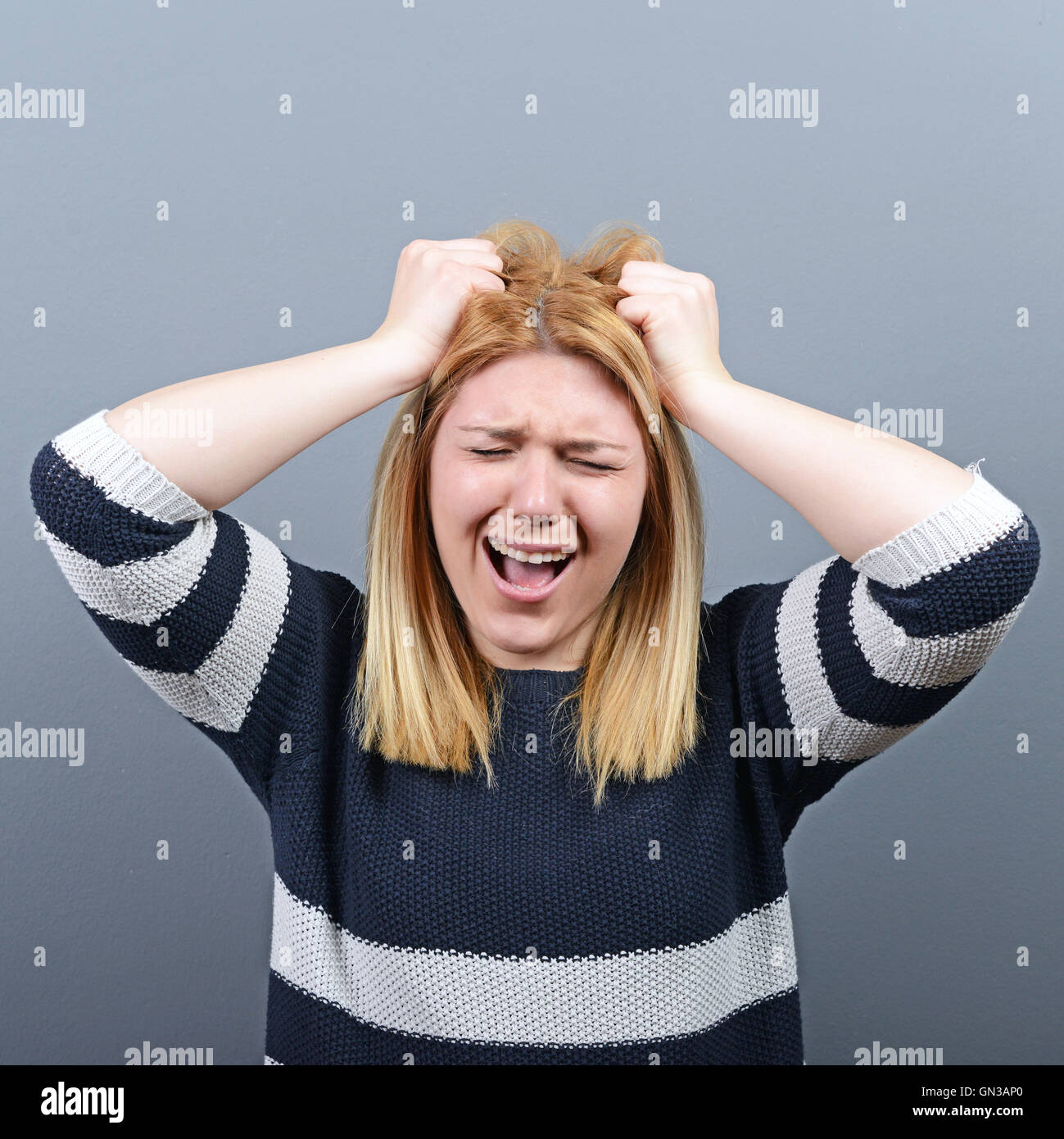 Portrait of a histerical woman pulling hair out against gray background