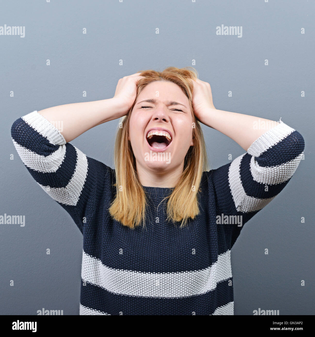 Portrait of a histerical woman pulling hair out against gray background