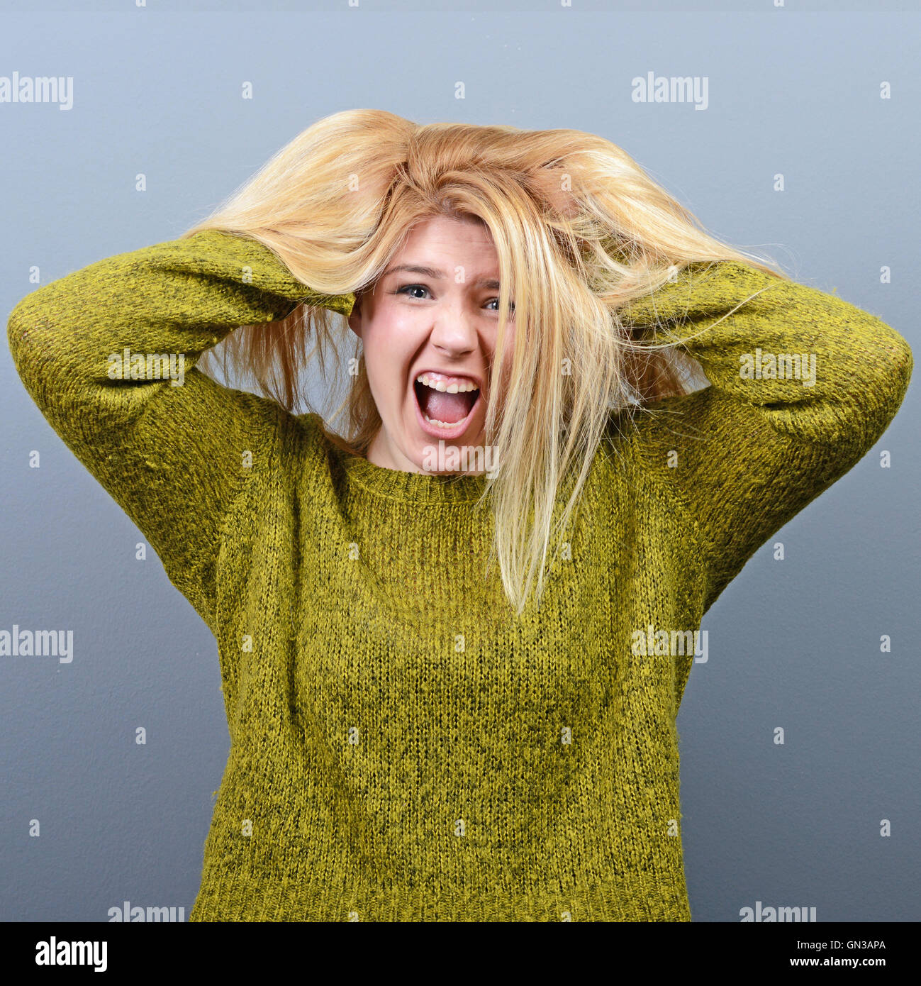Portrait of a histerical woman pulling hair out against gray background
